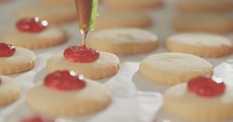 Close up of a baker piping strawberry jam on cookies.