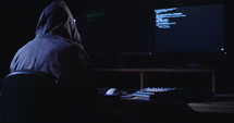 Computer hacker sitting in a dark room hacking security systems
