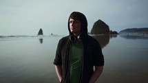 a man in a hoodie with headphones walking on a beach 