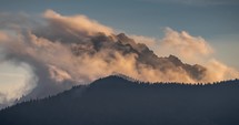 Misty clouds over alps mountains peak, evening light of sunset Timelapse
