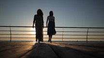Silhouettes of women goes on embankment to sea or ocean in sunrise light