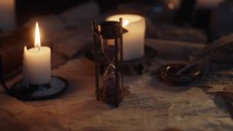 Panning shot of a desk with burning candles, scrolls, a quill, and an hourglass.