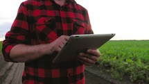 Farmer uses a tablet at sunset, plans to harvest. Tapping the tablet screen. The concept of technology in agriculture.