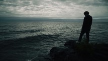 man standing on a rock on a shore looking out over the ocean 