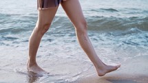 Legs of girl walking barefoot on wet sandy island beach. Slow motion.