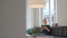 A woman sitting on a couch in front of a window reading a Bible 