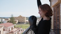 Woman Raises Her Fist In Victory With Boxing Gloves On The Balcony