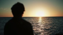 silhouette of a man standing on a shore looking out over the ocean at sunset 