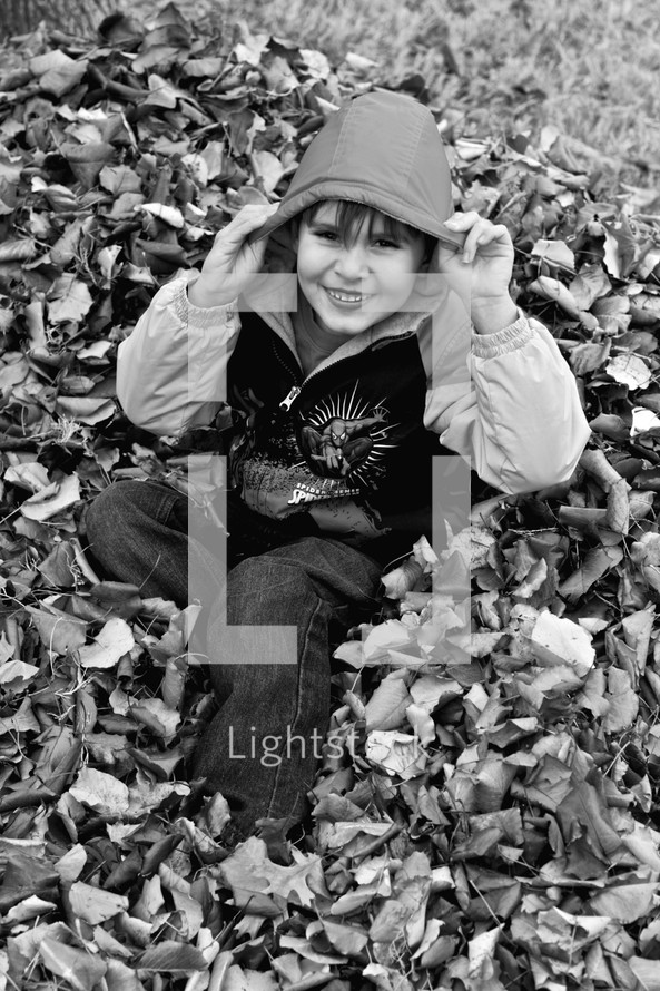 boy child playing in a leaf pile