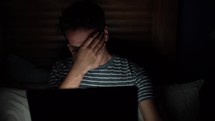 a man looking at a computer screen alone in a dark room 