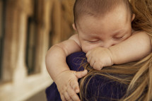 An infant sleeping on his mother's shoulder.