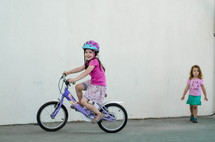 A little girl in a hamlet rides a purple bicycle.