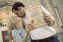 Newly married couple holding marriage certificate and kissing