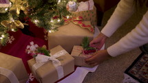 Woman placing a wrapped present under a Christmas tree.