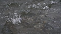 Slow motion of crystal clear water waves flowing in mountain stream river nature background
