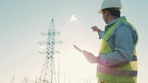 Engineer standing on field with electricity towers. Electrical engineer with high voltage electricity pylon at sunset background. Power workers at work concept.