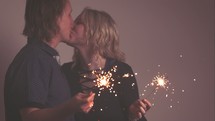 a couple holding sparklers and kissing 