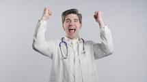 Mature physician man in white medical coat form shows triumph yes gesture of victory, he achieved result, goals. Healthcare specialist glad, happy, surprised excited happy on white. High quality 4k