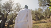 Scientist with lab coat walking and looking at olive trees