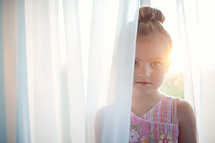 girl child standing in curtain sheers at a window