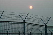 sun over a barbed wire lined fence