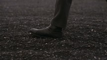 feet of a man walking across a barren flat landscape 