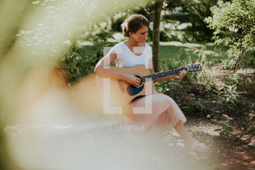 a woman sitting on a bench playing a guitar 