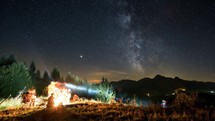 Friends sitting over campfire in starry night with milky way Time lapse
