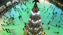 Festive city ice rink with people skating around Christmas tree