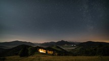 Stars moving in night sky over mountains and foggy rural landscape at moonlight. Night to day time-lapse dolly shot
