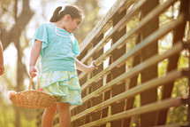 girl child holding a basket looking over the rails on a bridge