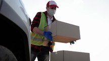 Delivery service. Delivery man in a protective mask and gloves near a car putting cardboard box into the trunk. Man open trunk car cardboard box parcel delivery transportation technology system.
