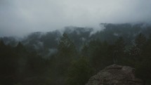 man standing on mountain looking out at clouds and fog over mountain tops 