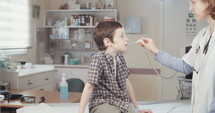 Female doctor checking a young boy's temperature using an oral thermometer in the clinic.