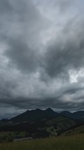 Vertical video of Dark dramatic clouds moving fast over mountains time lapse
