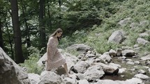 a woman in a dress walking across a stream outdoors 