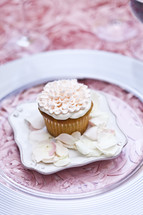 ornately decorated cupcake pink on plate with floral petals