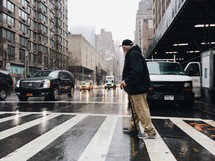 an elderly man with a cane using a crosswalk on a rainy day 