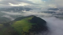 Aerial foggy country landscape in morning light above clouds with beautiful colors at sunrise. Tilt down on meadow and mist forest
