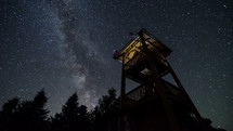 Stars sky with milky way turning over lookout tower time lapse. 