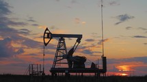 Silhouette working oil pump in deserted district at sunset. Oil drill rig and pump jack. Oil drilling derricks at desert oilfield for fossil fuels output and crude oil production from the ground.