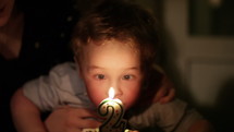Kid's birthday. Boy blows out the candle with number 2 in the cake.
