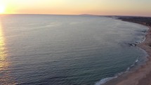 Sunset over ocean waves wash sand beach. 