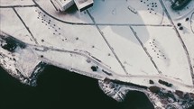 drone flying over a snowy shoreline and city roads 