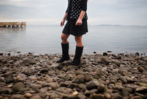 a woman in boots standing on a rocky beach 