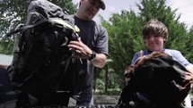 father and son unloading backpacks from car