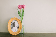A vase of pink tulips next to a framed photo of a mother and newborn baby.
