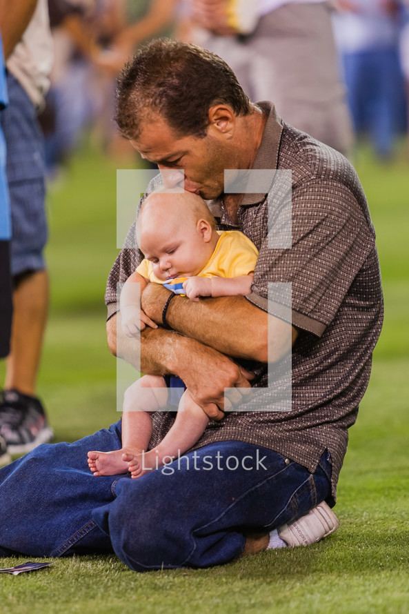 Man holding an infant child on knees praying at a crusade