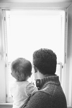 father and toddler son looking out a window 