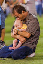 Man holding an infant child on knees praying at a crusade
